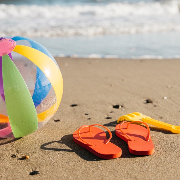 Slippers en opblaasbare bal in het zand op het strand