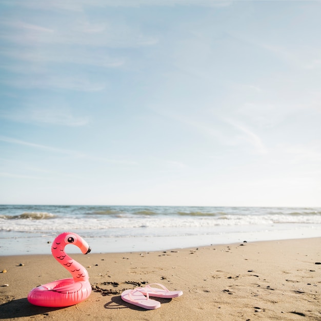 Slippers en opblaasbare flamingo op het strand