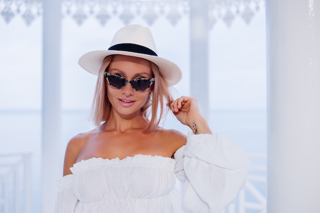 Sluit buiten mode portret van stijlvolle vrouw in volumineuze witte trendy top en klassieke luxe hoed en luipaard zonnebril