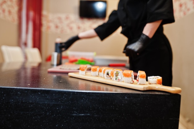 Sluit de handen van professionele chef-koks in zwarte handschoenen die sushi en broodjes maken in een restaurantkeuken van japans traditioneel eten
