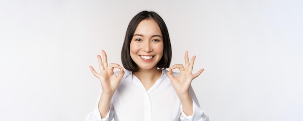Sluit het hoofdportret van een Aziatisch meisje dat een goed teken toont en tevreden glimlacht en adviseert om blij te zijn lof en een compliment te maken op een witte achtergrond
