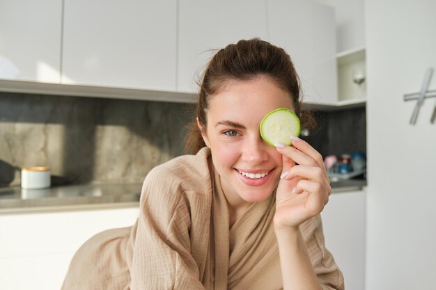 Gratis foto sluit het portret van een gelukkig mooi meisje dat courgette hakt en glimlachend poseert in de keuken