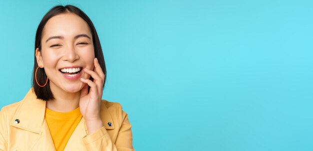 Sluit het portret van een natuurlijk Aziatisch meisje dat lacht en lacht en er gelukkig uitziet terwijl ze over een blauwe achtergrond staat