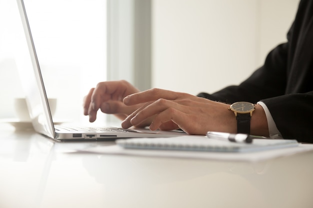 Sluit omhoog beeld van man indient polshorloge het typen op laptop