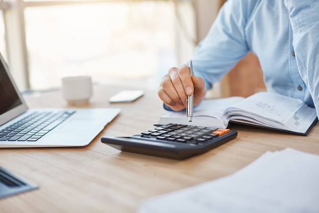 Sluit omhoog detail die van professionele ernstige accountantszitting in licht bureau, de winsten van bedrijffinanciën op calculator controleren