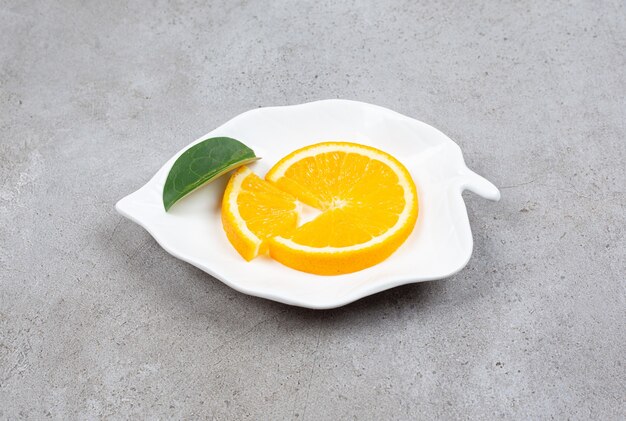 Sluit omhoog foto van sinaasappelplak met blad op witte plaat in bladvorm.