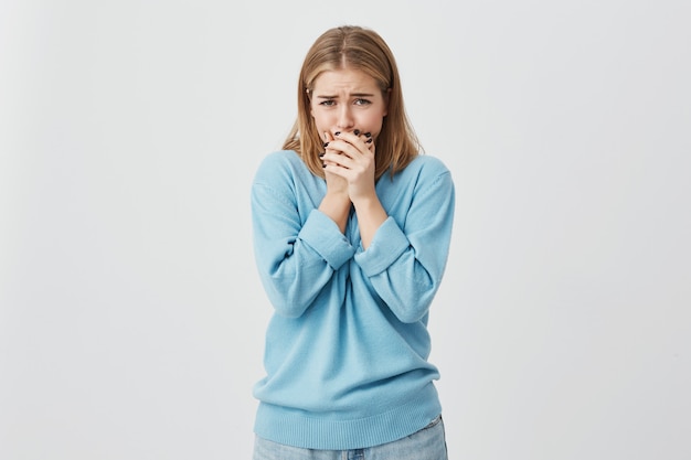 Sluit omhoog geschoten van verstoorde tiener die blauwe sweater en jeans dragen die bijna huilen, verbergend haar gezicht, absoluut geschokt door het slechte nieuws.