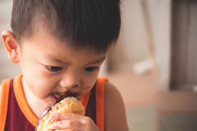 Sluit omhoog gezicht van hongerige kleine jongen eaitng hete doughnut