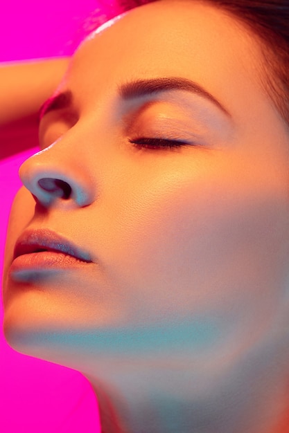 Sluit omhoog het portret van de Kaukasische die vrouw op roze studioachtergrond in gemengd neonlicht wordt geïsoleerd. Mooi vrouwelijk model. Concept van menselijke emoties, gezichtsuitdrukking, verkoop, advertentie, mode. Schoonheid.