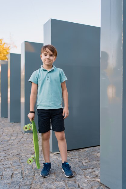 Sluit omhoog jongen die blauwe tennisschoenen dragen oefenend met groen skateboard. Actieve stedelijke levensstijl van jeugd, opleiding, hobby, activiteit. Actieve buitensport voor kinderen. Kind skateboarden.