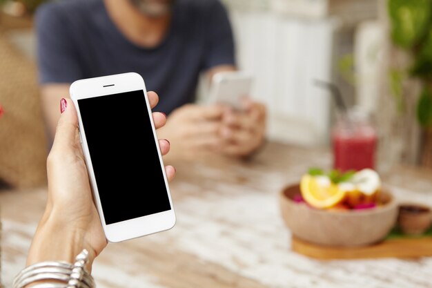 Sluit omhoog mening van de handen van de vrouw met rode spijkers dragend modieuze armband houdend mobiele telefoon