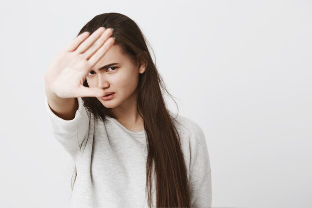 Sluit omhoog mening van tienervrouw die met donker lang haar eindegebaar met hand maken, fronsend gezicht.