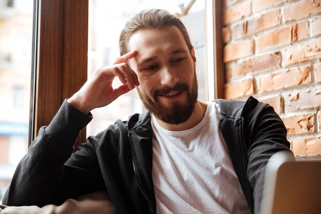 Sluit omhoog portret van de Gebaarde mens gebruikend laptop in koffie