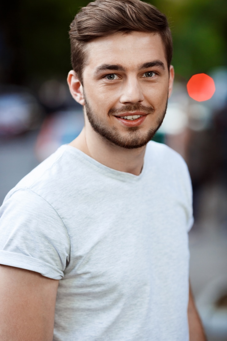 Gratis Foto sluit omhoog portret van de knappe glimlachende jonge mens in witte t-shirt op onscherpe openluchtaard