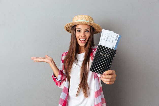 Sluit omhoog portret van een glimlachende gelukkige vrouwenreiziger in strohoed die paspoort met vliegtuigkaartjes tonen