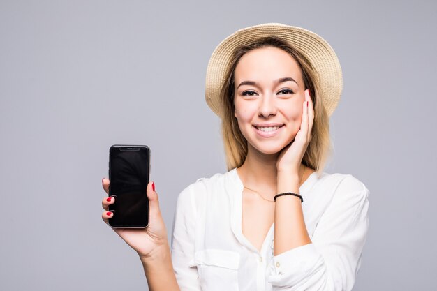 Sluit omhoog portret van een glimlachende vrouw die een lege scherm mobiele telefoon toont terwijl status geïsoleerd over grijze muur