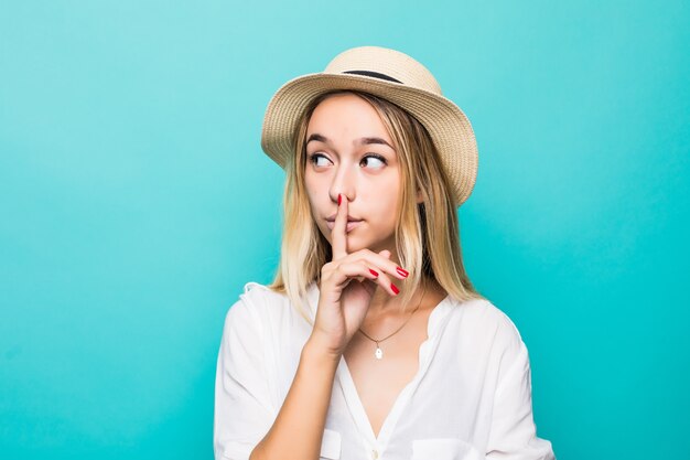 Sluit omhoog portret van een jonge vrouw die stiltegebaar toont dat over blauwe muur wordt geïsoleerd