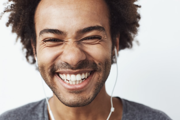 Sluit omhoog portret van het jonge gelukkige Afrikaanse mens glimlachen luisterend aan het vrolijke streaming muziek lachen. Jeugd concept.