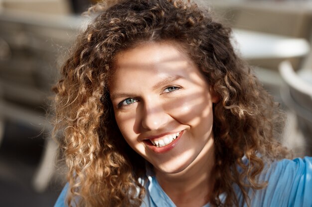 Sluit omhoog portret van jonge mooie glimlachende meisjeszitting bij koffie in zonnestralen.