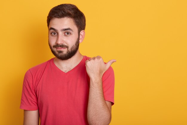 Sluit omhoog portret van knap jong mannetje die met baard opzij met duim richten