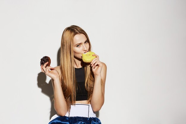 Sluit omhoog portret van knappe blondevrouw in de holding van de sportslijtage donuts in handen, met flirty en uitdrukking.