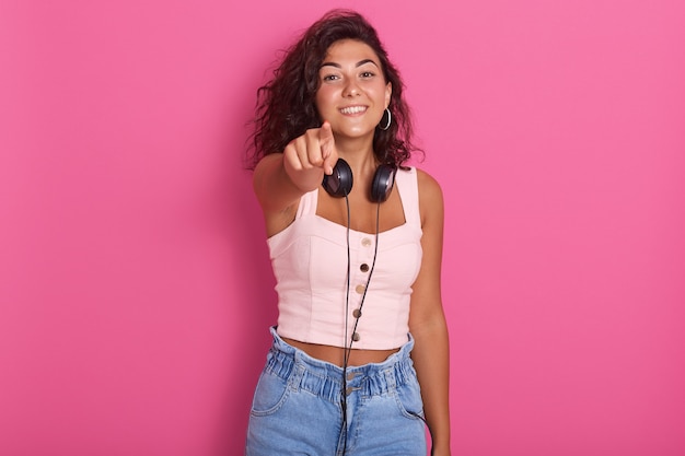 Sluit omhoog portret van mooi meisje die met haar wijsvinger naar camera poiting, charmant vrouwelijk dragend roze bovenkant en jeans