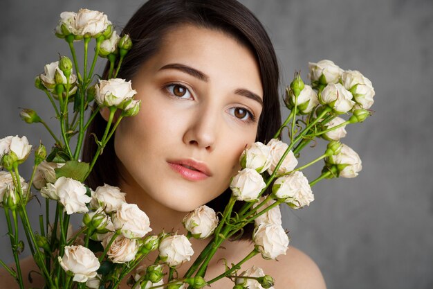 Sluit omhoog portret van tedere jonge vrouw met bloemen over grijze muur