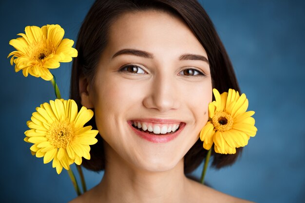 Sluit omhoog portret van tedere jonge vrouw met gele bloemen over blauwe muur