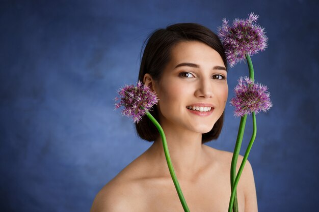 Sluit omhoog portret van tedere jonge vrouw met lila bloemen over blauwe muur