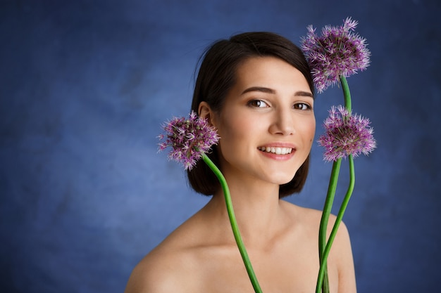 Sluit omhoog portret van tedere jonge vrouw met lila bloemen over blauwe muur
