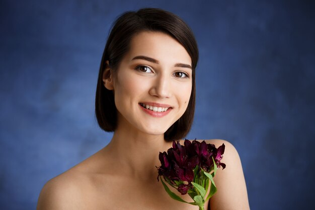 Sluit omhoog portret van tedere jonge vrouw met rode bloemen over blauwe muur