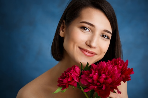 Sluit omhoog portret van tedere jonge vrouw met rode bloemen over blauwe muur