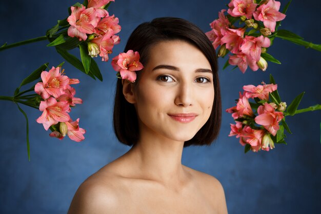 Sluit omhoog portret van tedere jonge vrouw met roze bloemen over blauwe muur