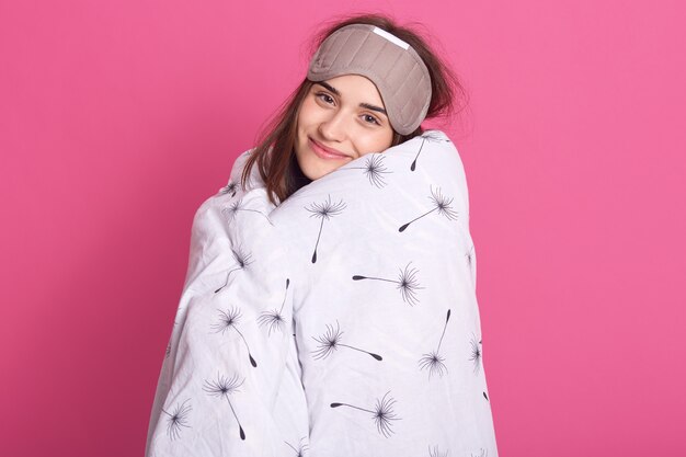 Sluit omhoog portret van vrouw met slaapmasker op hoofd en het dragen van deken bekijkend glimlachend camera