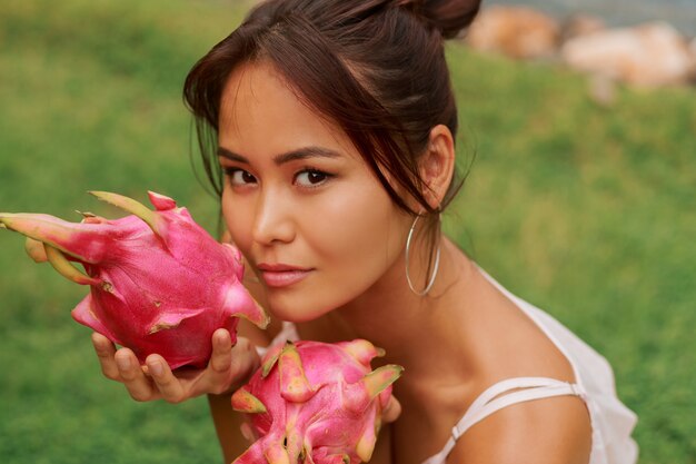 Sluit omhoog schoonheidsportret van vrij Aziatische vrouw met draakfruit naast gezicht.