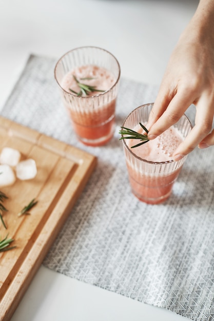 Gratis foto sluit omhoog van de handen van de vrouw verfraaiend grapefruit detox gezonde smoothie met rozemarijn.