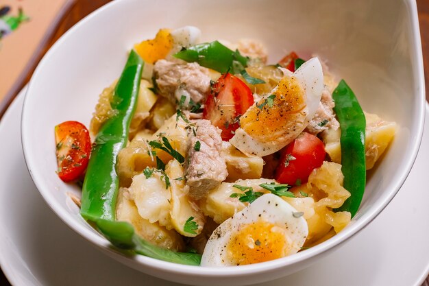 Sluit omhoog van de Italiaanse kom van de aardappelsalade met van de de kersentomaat van tonijnbonen de peterselie gekookte eieren en olijfolie