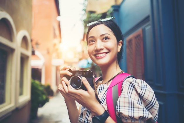 Sluit omhoog van de jonge rugzak die van de hipstervrouw reizende foto met haar camera in stedelijk berijden.