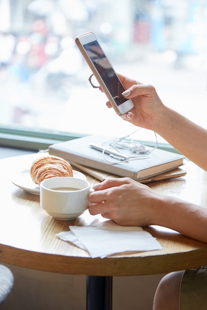 Sluit omhoog van onherkenbare vrouwelijke handen houdend de telefoon en de kop van koffie