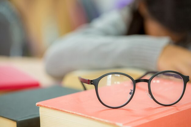 Sluit omhoog van oogglazen op houten bureau en handboek in bibliotheek.