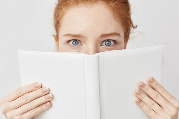 Sluit omhoog van roodharigevrouw met blauwe ogen achter boek.