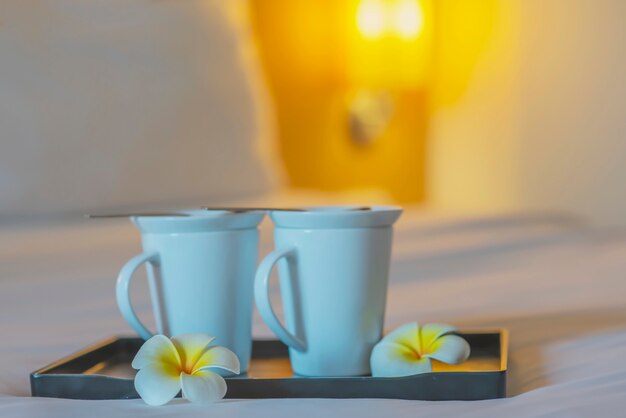 Sluit omhoog van tweeling welkome koffiekop op wit bed in hotelruimte - het concept van de de vakantiereis van de hotelkoffie