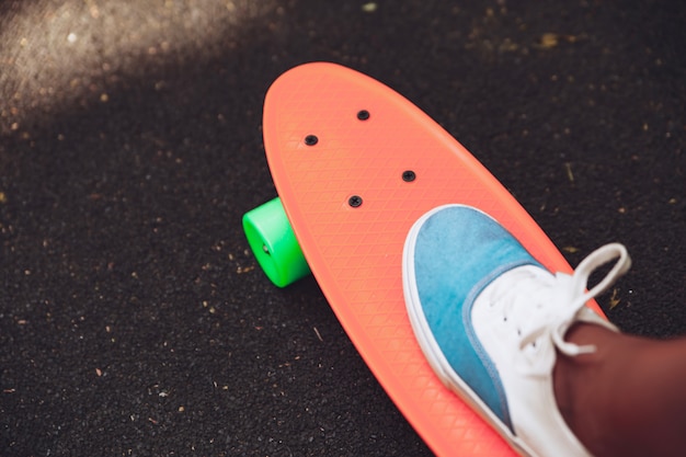 Sluit omhoog van voeten ritten van meisjessneakers op oranje stuiverskateboard op asfalt