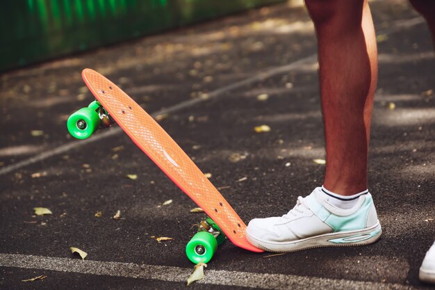 Sluit omhoog van voeten ritten van mensentennisschoenen op oranje stuiverskateboard op asfalt