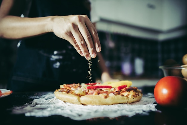 Sluit omhoog van vrouwenhand die orego over tomaat en mozarella op een pizza zetten.