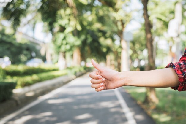 Sluit omhoog vrouwenhand lift bij plattelandsweg dichtbij bos, alleen reis