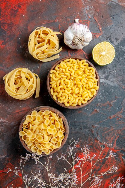 Smakelijke dinerbereiding met ongekookte pasta's in verschillende vormen en knoflook op gemengde kleurenachtergrond