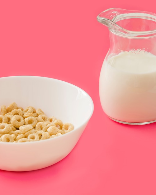 Smakelijke maïs ringen in de witte kom met melkkannetje op donker roze achtergrond