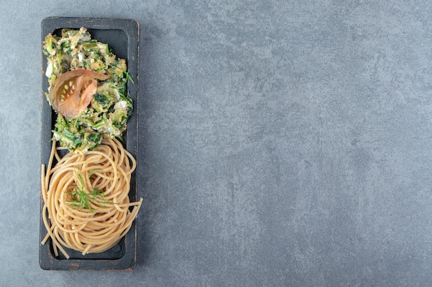 Smakelijke omelet met greens en spaghetti op zwarte plaat.