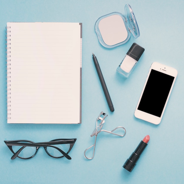 Smartphone met notitieboekje en schoonheidsmiddelen op blauwe lijst